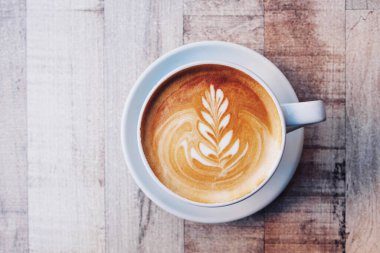 Bir fincan taze kapuçino ve ahşap arka planda güzel latte sanat eserleri, yakın plan. Yukarıdan, boşluğu kopyala.