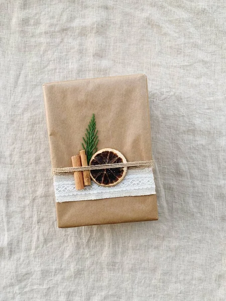 Christmas gift box wrapped with brown paper and decorated with dry orange slice, cinnamon sticks and fit branch, top view. Zero waste holiday concept. Eco friendly and plastic free gift wrapping.