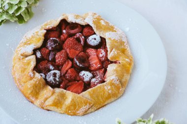 Beyaz zemin üzerinde taze pişmiş vegan çilek ve kiraz galeti ve ortanca çiçekleri, yakından. Tatlı yemek, yaz tatlısı..