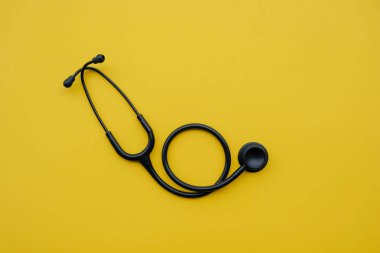 Sarı arka planda siyah tıbbi steteskop. Tıp ve sağlık hizmetleri kavramı. Mesaj için yer var. Düz-yatay, üst görünüm.