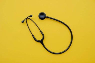 Sarı arka planda siyah tıbbi steteskop. Tıp ve sağlık hizmetleri kavramı. Mesaj için yer var. Düz-yatay, üst görünüm.