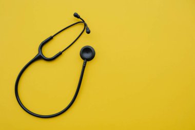 Sarı arka planda siyah tıbbi steteskop. Tıp ve sağlık hizmetleri kavramı. Mesaj için yer var. Düz-yatay, üst görünüm.