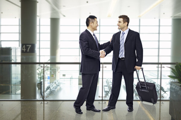 бизнесмены пожимают руки в аэропорту
