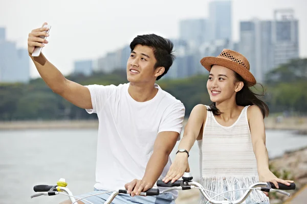 Jovem asiático casal equitação bicicleta e tomando um selfie — Fotografia de Stock