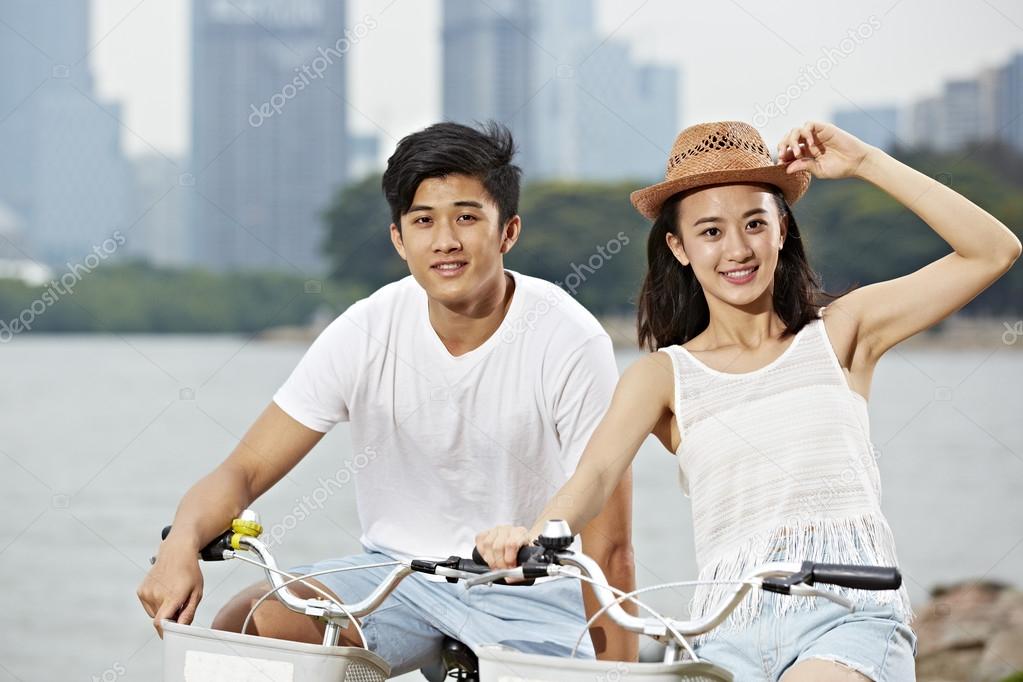 young asian couple riding bike in city park