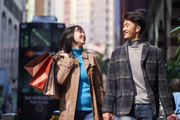 happy and loving young asian couple walking on street with shopping bags in hand