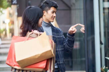 Modern şehirde alışveriş yaparken dükkan vitrinine bakan mutlu Asyalı çift.