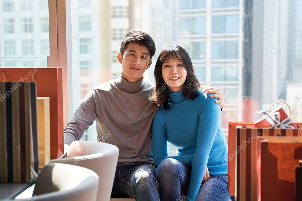 young asian couple resting and relaxing sitting by window in hotel room after shopping in the city