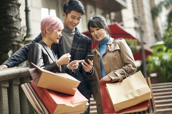 3人の若いアジア系ファッショナブルな人が街で買い物をしながら携帯電話を — ストック写真