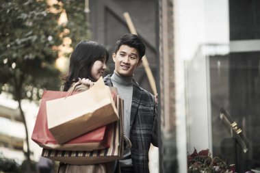 Şehirde ellerinde alışveriş torbalarıyla dolaşan mutlu Asyalı genç çift.