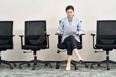 Genç Asyalı kadın iş arayan sandalyede oturmuş sırada beklerken röportaj için hazırlanıyor.