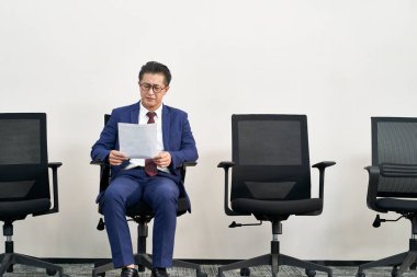 mature asian male job seeker preparing for interview while waiting in line clipart