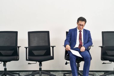 Sandalyede oturan yaşlı Asyalı iş arayan hayal kırıklığına uğramış ve mağlup olmuş görünüyor.