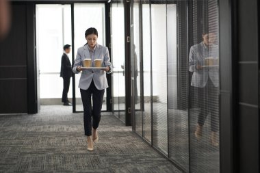 Genç Asyalı stajyer stajyer şirket ofisinde bir tepsi kahve taşıyor.