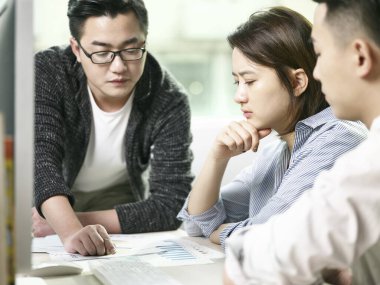 Asyalı erkek ve kadın takımları ofiste iş konuşuyorlar.