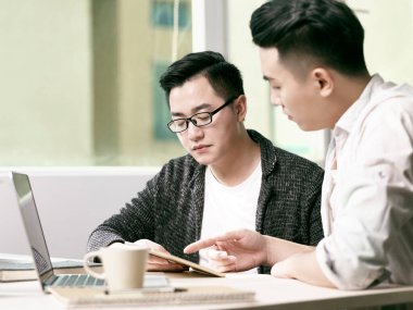 İki genç Asyalı girişimci dijital tablet ve dizüstü bilgisayar kullanarak ofiste iş konuşuyorlar