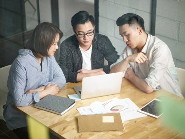 Üç Asyalı girişimci ofiste toplanıp laptopla iş konuşuyorlar.