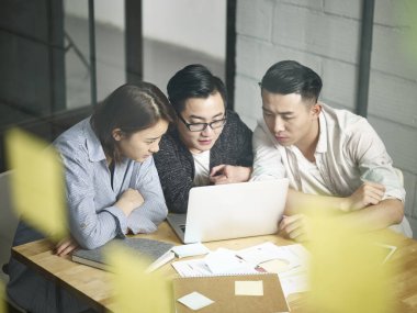 Üç Asyalı girişimci ofiste toplanıp laptopla iş konuşuyorlar.