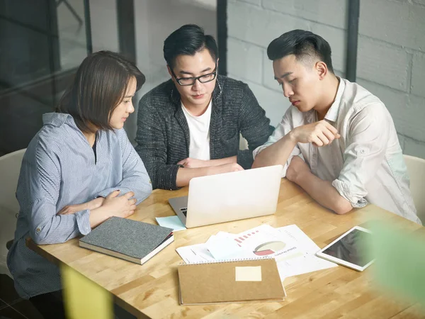 Üç Asyalı girişimci ofiste toplanıp laptopla iş konuşuyorlar.