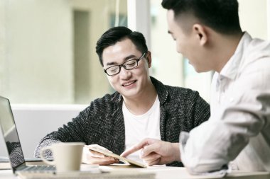 İki genç Asyalı girişimci dijital tablet ve dizüstü bilgisayar kullanarak ofiste iş konuşuyorlar