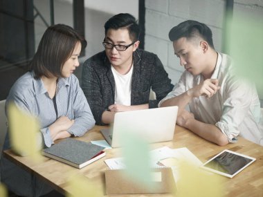 Ofiste birlikte çalışan üç Asyalı genç girişimci iş planını dizüstü bilgisayarla tartışıyor.