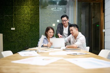 Üç Asyalı girişimci ofiste toplanıp laptopla iş konuşuyorlar.