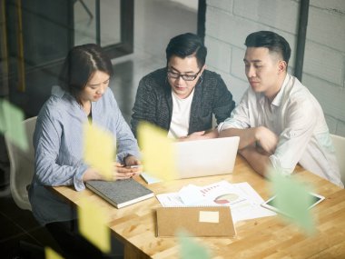 Üç Asyalı girişimci ofiste toplanıp laptopla iş konuşuyorlar.