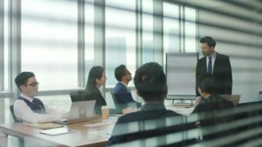 Asyalı iş adamlarından oluşan bir ekibin cam ve perdeleri ardında modern ofis konferans salonunda buluşan erkek ve kadınlar.