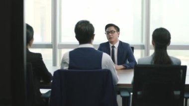 Modern şirketin konferans odasında bir grup İK yöneticisi tarafından sorgulanan kibirli Asyalı genç iş adamı.