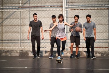 Genç Asyalı kaykaycı kız arkadaşlarıyla dışarıda kaykay yapıyor.