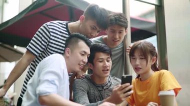 Bir grup Asyalı yetişkin birlikte cep telefonuna bakıp mutlu ve gülümsüyor.