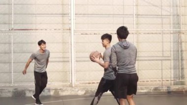Genç Asyalı yetişkin erkekler dışarıda basketbol oynuyorlar.