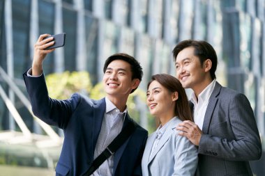 Asyalı iş adamlarından oluşan bir ekip modern şehrin finans bölgesinde selfie çekiyor.