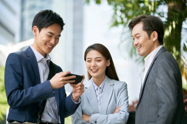 Üç Asyalı iş ortağı modern şehrin şehir merkezindeki finans bölgesinin caddesinde sohbet ediyorlar.