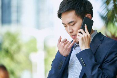 Genç Asyalı işadamı dışarıda cep telefonuyla konuşuyor.