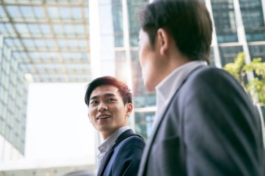 two asian business people walking talking on street in modern city