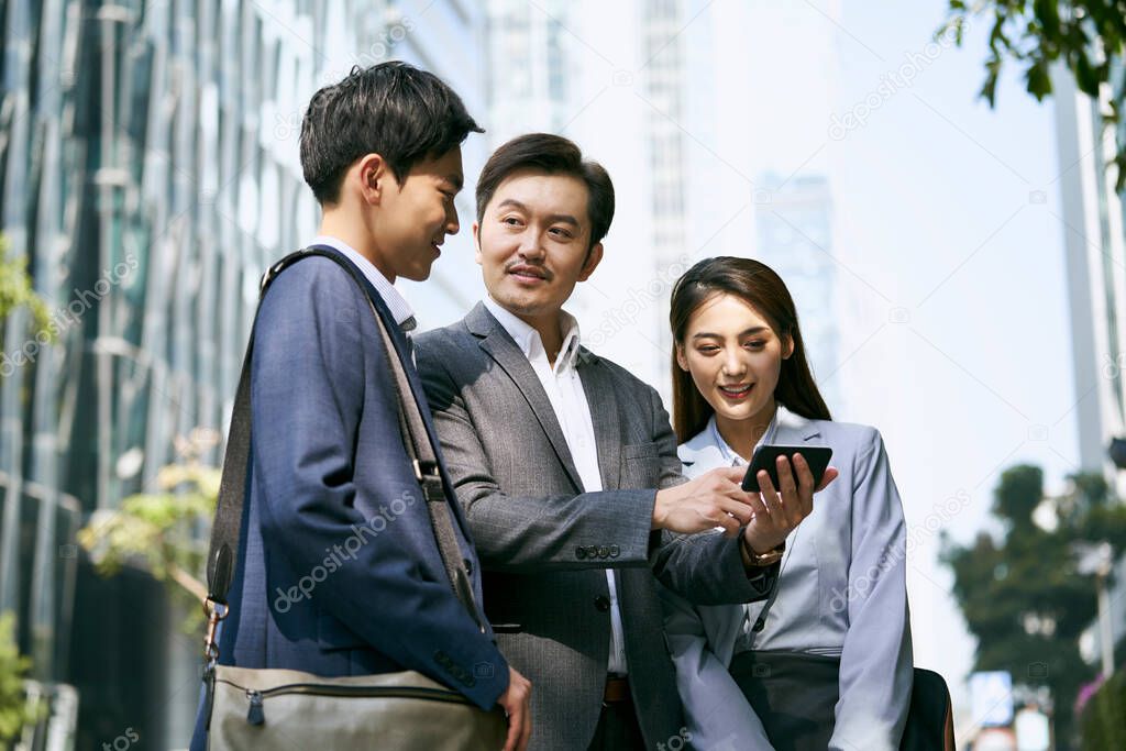 a team of asian business people standing in street having a discussion using cellphone in city downtown