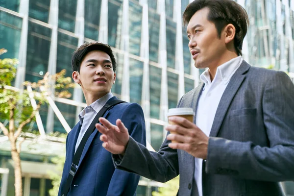两个亚洲企业高管一边在现代城市的商业区街上散步一边谈论业务的侧视图 — 图库照片
