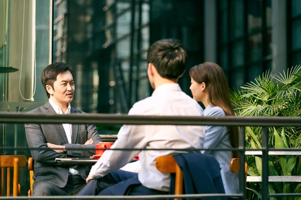 three asian corporate businesspeople discussing business outdoors in coffee shot