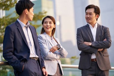 Üç mutlu Asyalı iş adamı dışarıda iş konuşarak sohbet ediyorlar.