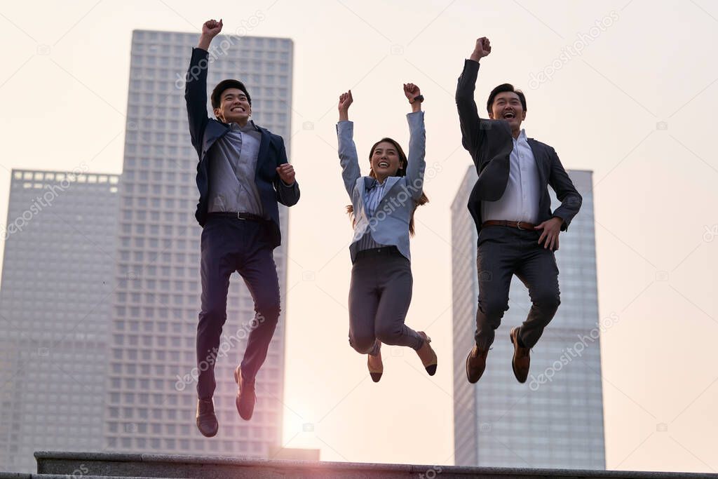 team of three asian corporate executives jumping celebrating success and achievement with city background