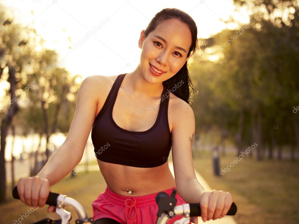 young asian woman riding bike outdoors at sunset