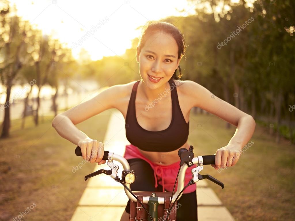 young asian woman riding bike outdoors at sunset
