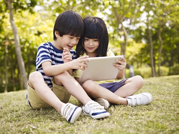 Twee Aziatische kinderen met behulp van tablet buitenshuis — Stockfoto