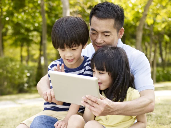 Азиатский отец и дети с помощью планшета на открытом воздухе — стоковое фото