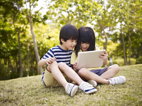 Twee Aziatische kinderen met behulp van tablet buitenshuis — Stockfoto