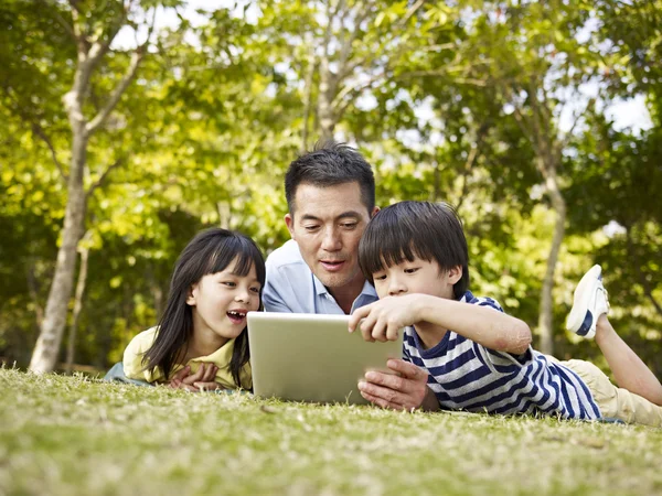 Asiático padre y niños usando tableta ordenador al aire libre —  Fotos de Stock