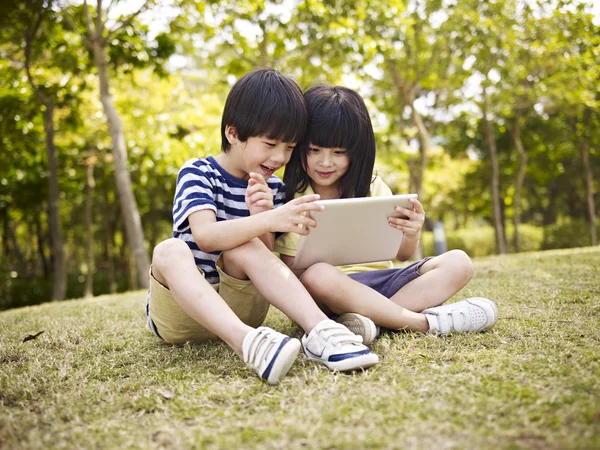 Dos asiático niños usando tableta al aire libre —  Fotos de Stock