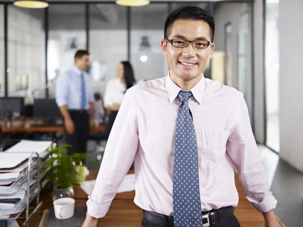 Asian businessman standing in office arms crossed with multinati — Stock Photo, Image