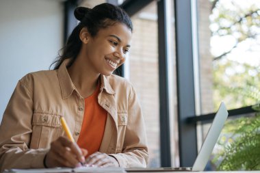 Üniversite öğrencisi dizüstü bilgisayar kullanıyor, çalışıyor, not alıyor, internetten öğreniyor. Ofiste çalışan gülümseyen iş kadını. 